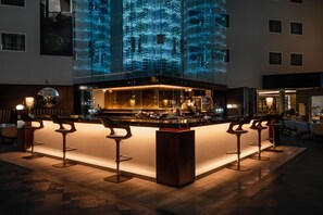 A bar area with a modern design, featuring a bar counter and multiple stools.