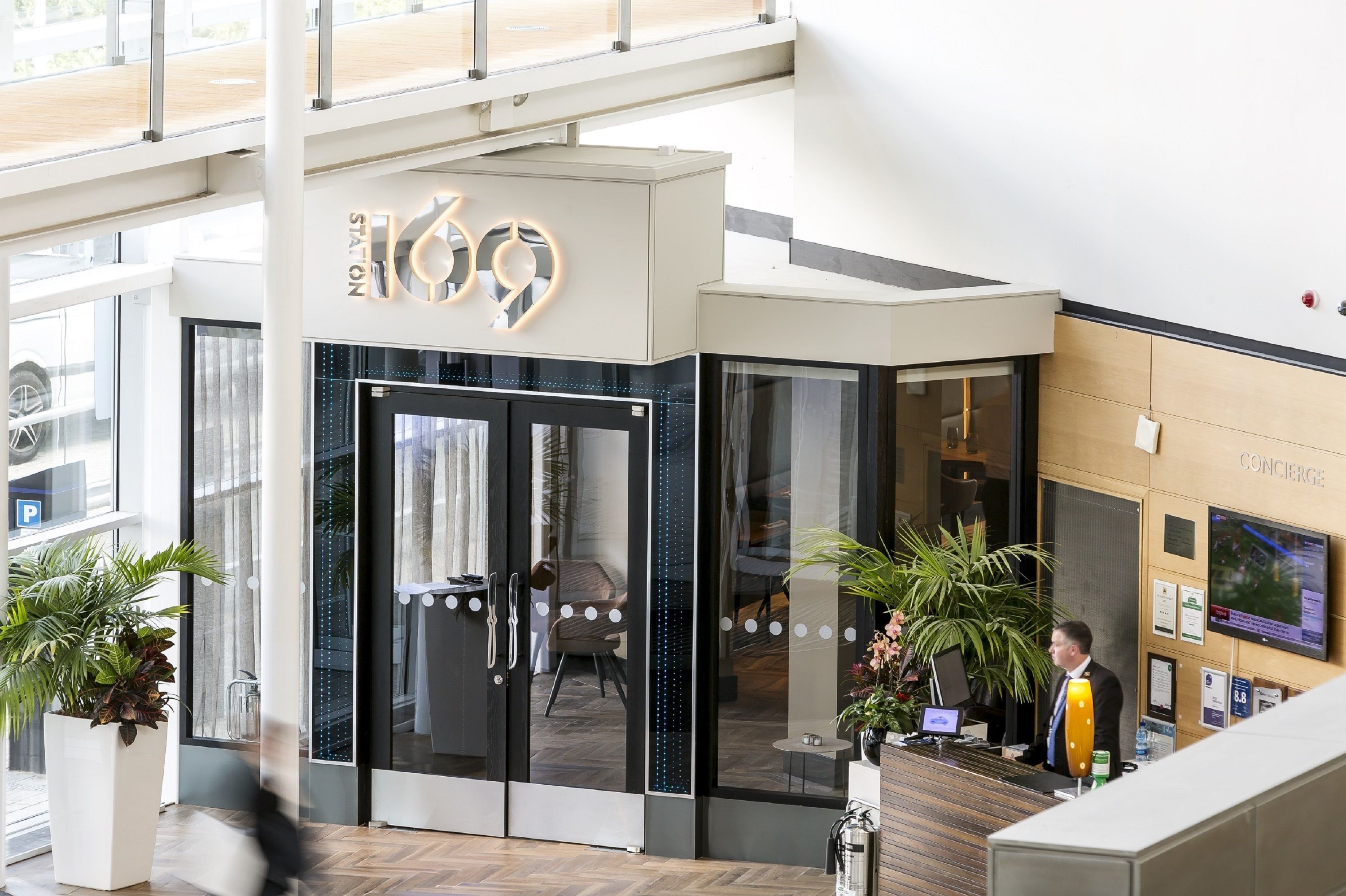 Un rebedor d'hotel modern, amb taulell de recepció, portes de vidre i zona de consergeria.