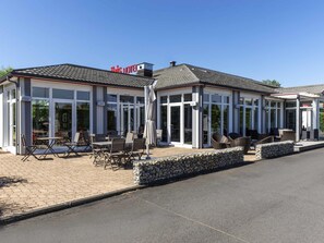 A hotel with a covered outdoor seating area, a stone wall, and a clear blue sky. - ibis Issoire (Issoire)