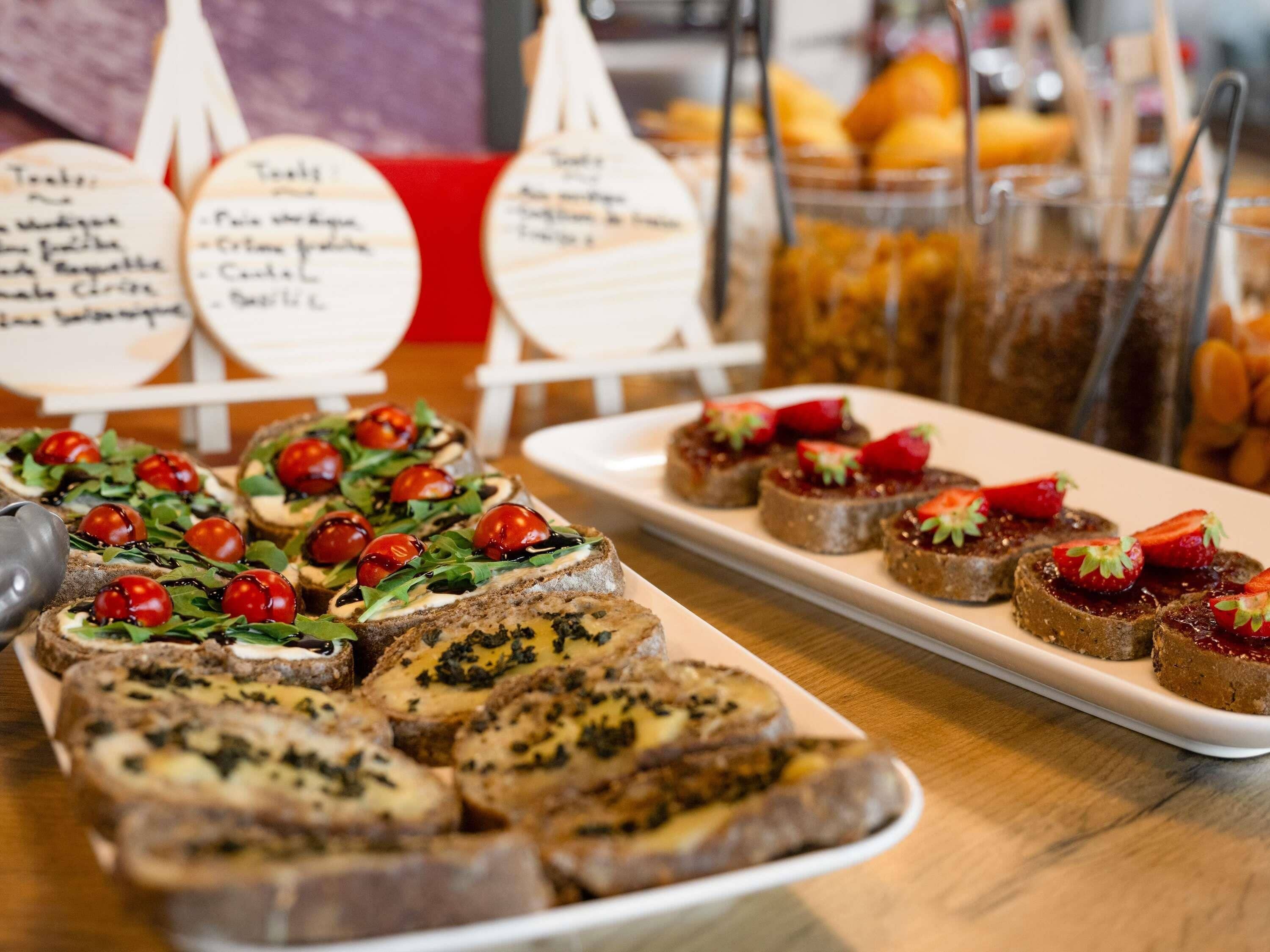 Ein reichhaltiges Buffet mit verschiedenen Speisen, darunter Brot mit Belägen, eine Obstauslage und ein Schild mit Menüauswahl.