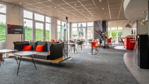 A modern interior with a sofa, tables, and chairs, large windows, and a sign for 'ibis MUSIC'.