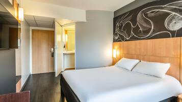 A hotel room with a large bed, a wooden headboard, a wall-mounted artwork, and a door leading to a bathroom.
