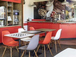A modern kitchen with red cabinets, a coffee machine, and a dining area with a chessboard. - ibis Issoire (Issoire)