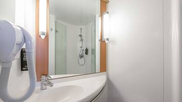 A bathroom with a white sink, a mirror, a handheld showerhead, and a hairdryer.