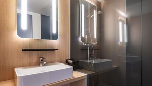 A modern bathroom with a large mirror, a white sink, and a glass shower enclosure.