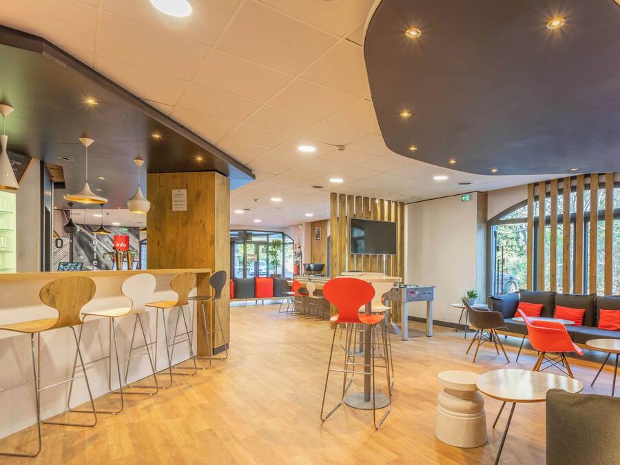 Un café moderno con suelo de madera, taburetes de bar, sillas rojas y una zona de estar con sofás y mesas.