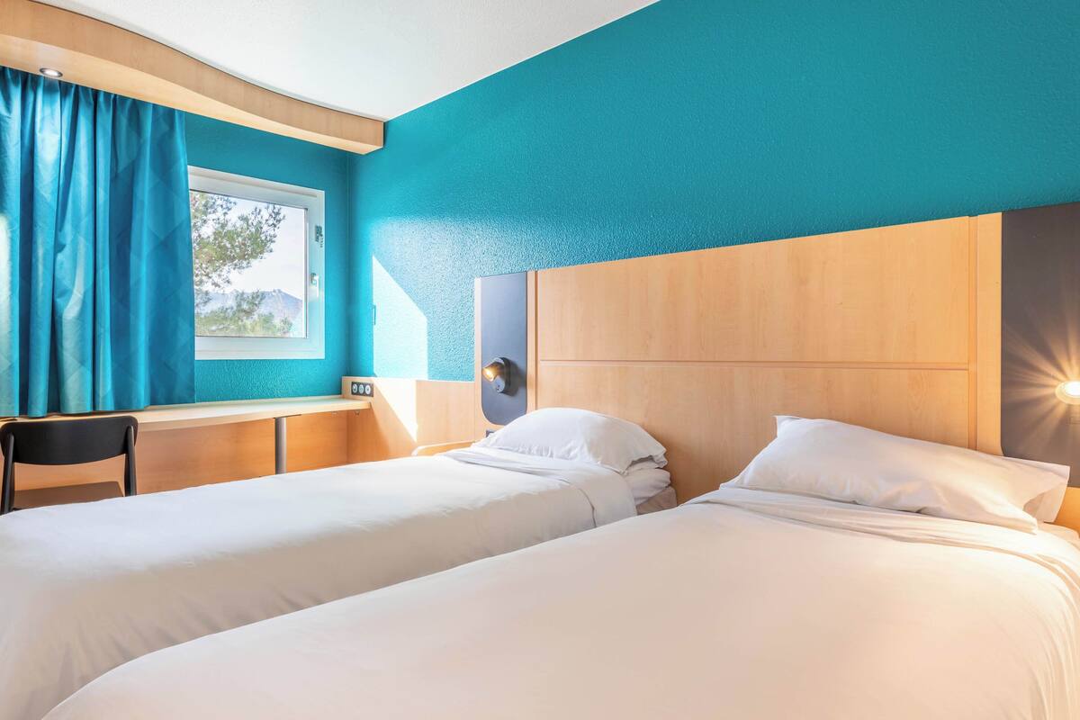 A hotel room with two beds, a desk, and a window with curtains.