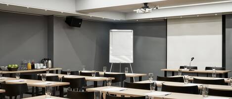 Una sala de conferencias con varias mesas, sillas, un proyector y una pizarra.