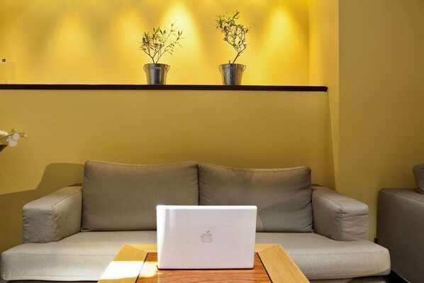 A modern living room with a sofa, a laptop on a wooden table, and two potted plants on a shelf.