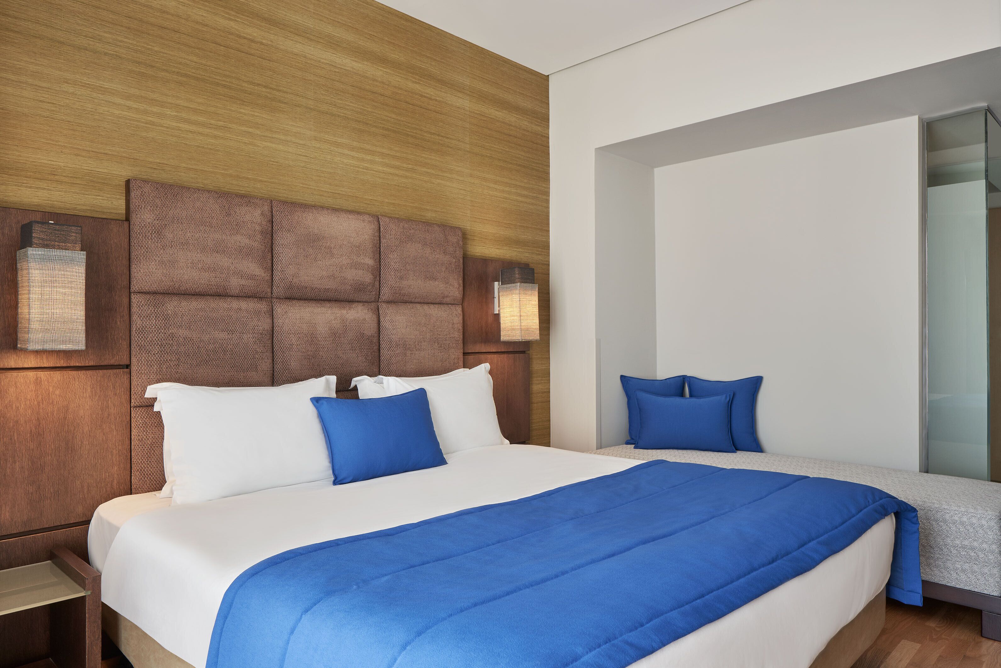 A hotel room with a large bed, a wooden headboard, and a small bedside table.
