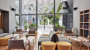 A modern interior with a large window, seating area, and a bookshelf. - Arion Athens Hotel (Athens)