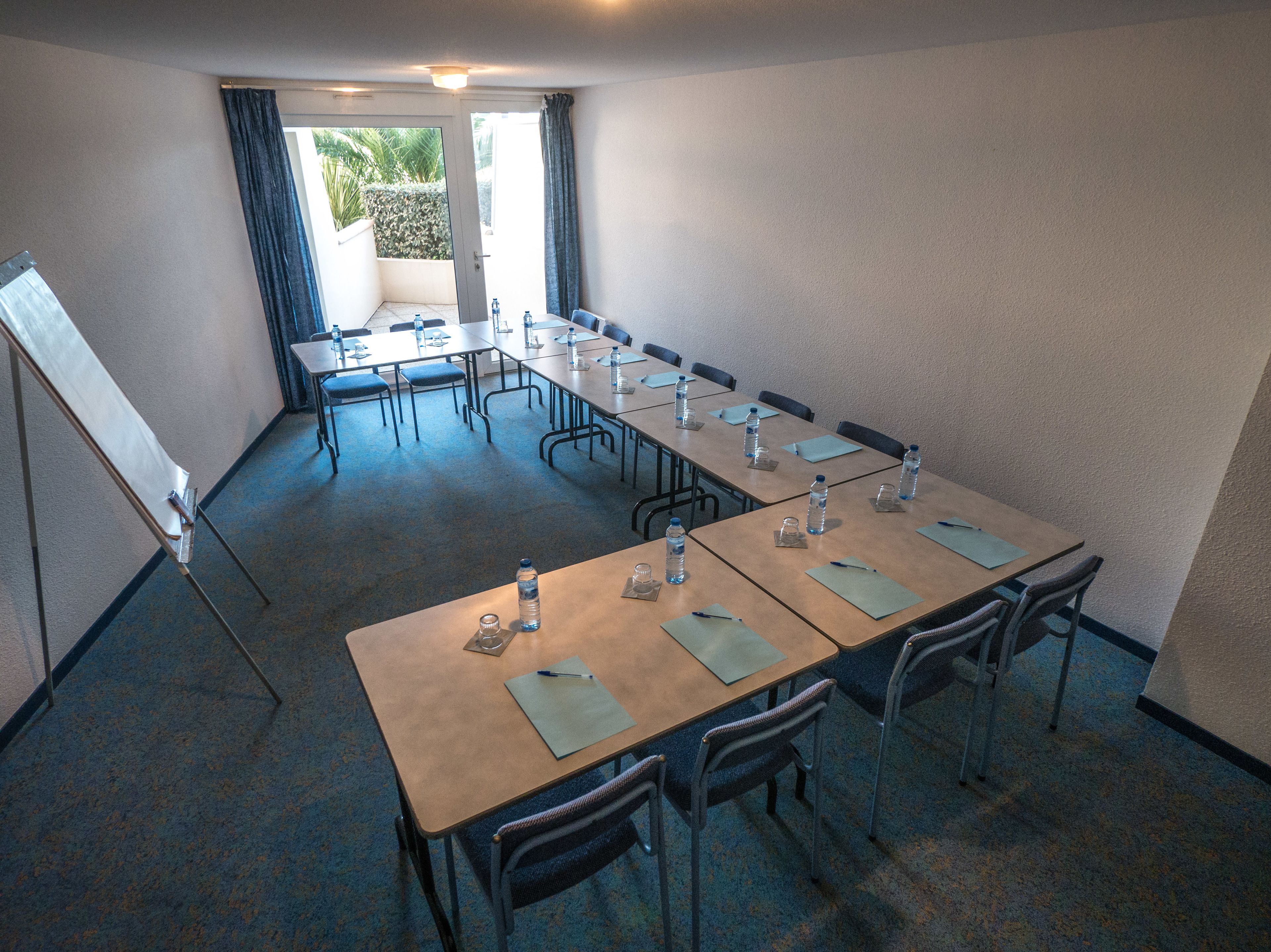 Une salle de conférence équipée de longues tables, de chaises, de bouteilles d’eau et d’un tableau blanc.