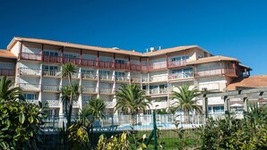 A multi-story hotel with balconies, a swimming pool, and palm trees. - Résidence Le Boucanier (Vieux-Boucau-les-Bains)