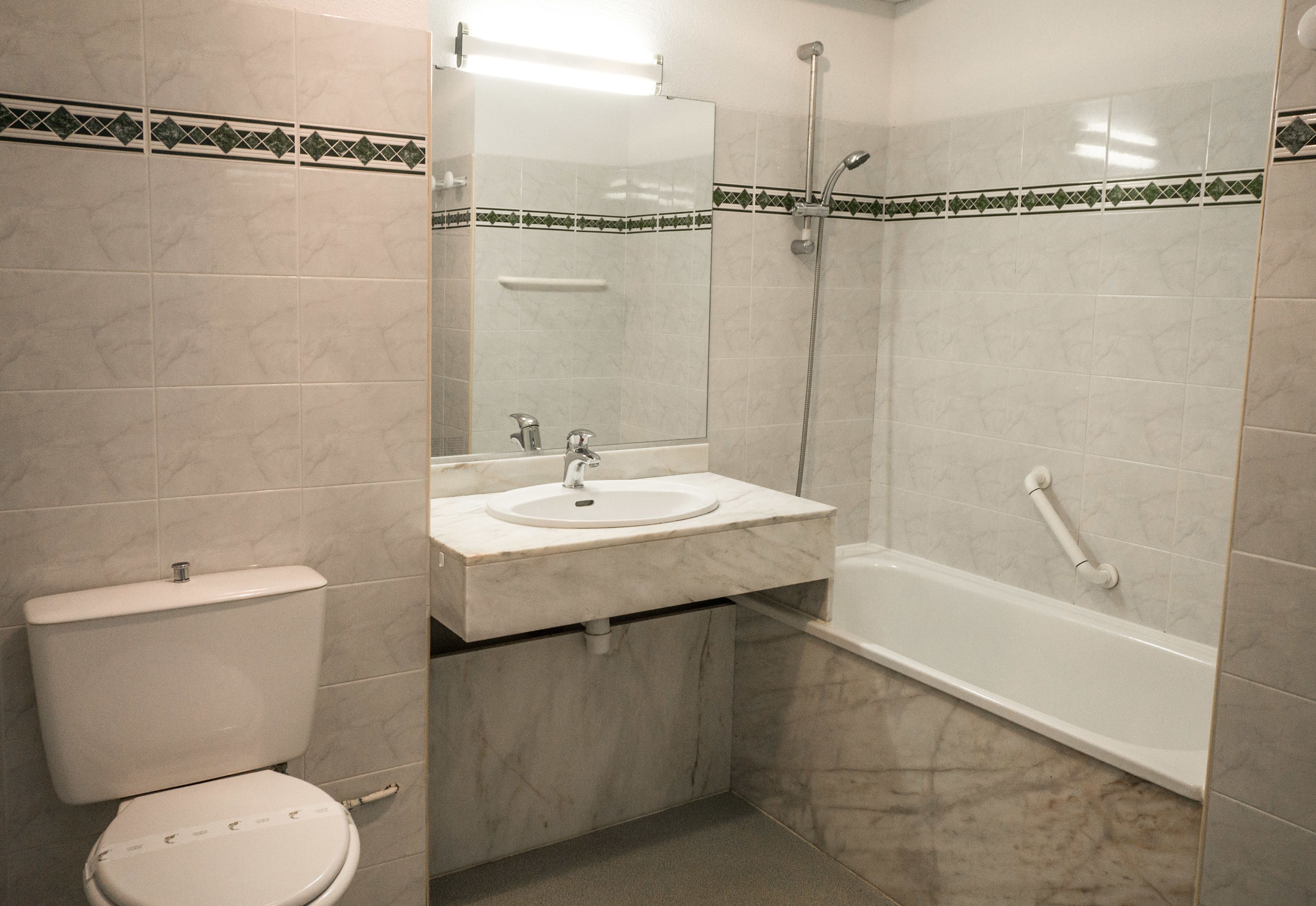 A bathroom with a toilet, sink, mirror, and bathtub.