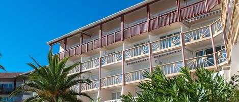 Un hotel a più piani con balconi, palme e cielo azzurro.