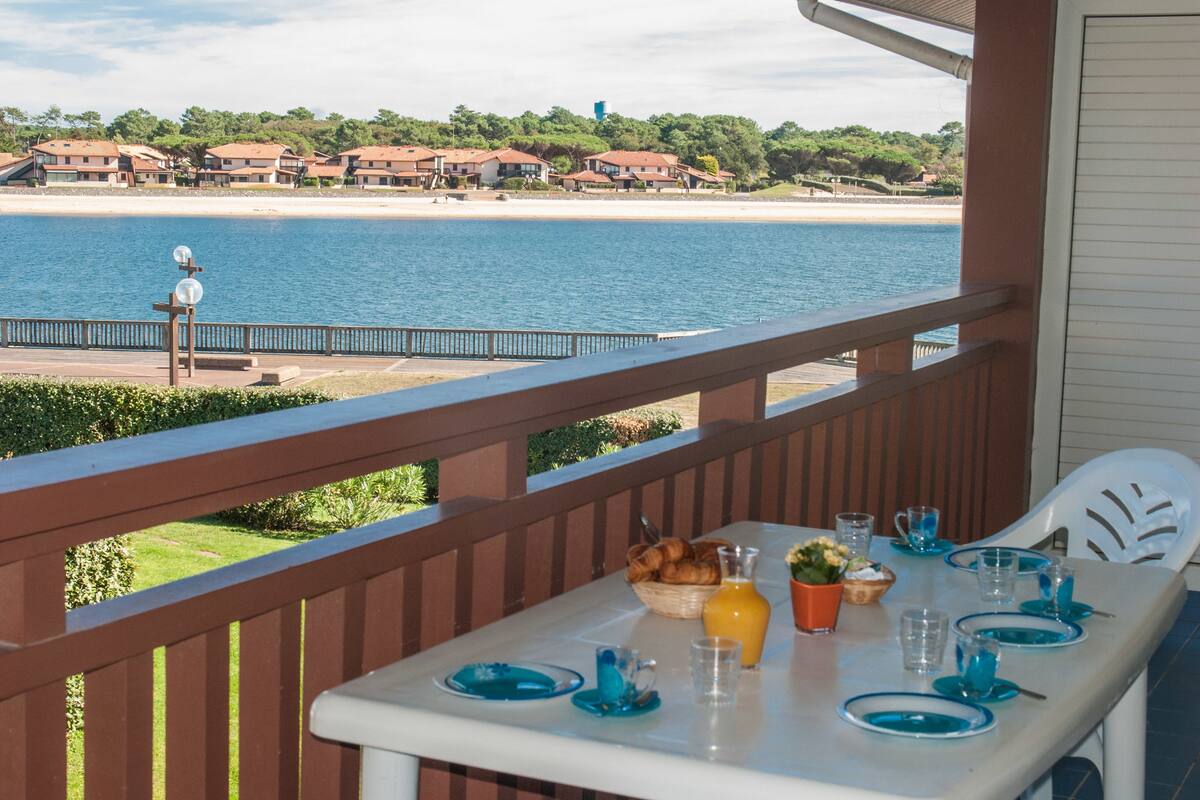A table set on a balcony overlooking a beach with houses in the background.
