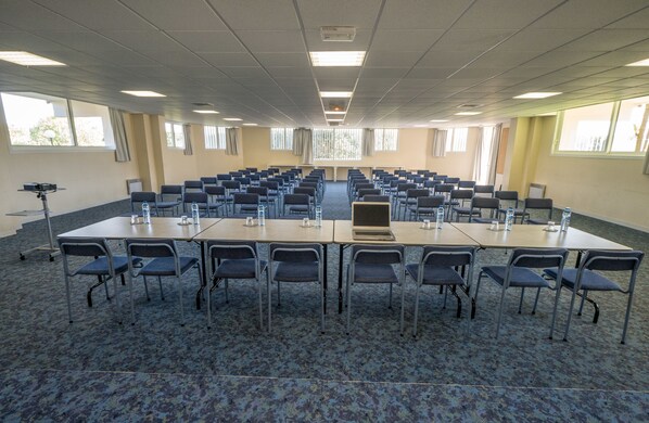 Un salón de conferencias con varias mesas y sillas, equipado con botellas de agua y una computadora portátil.