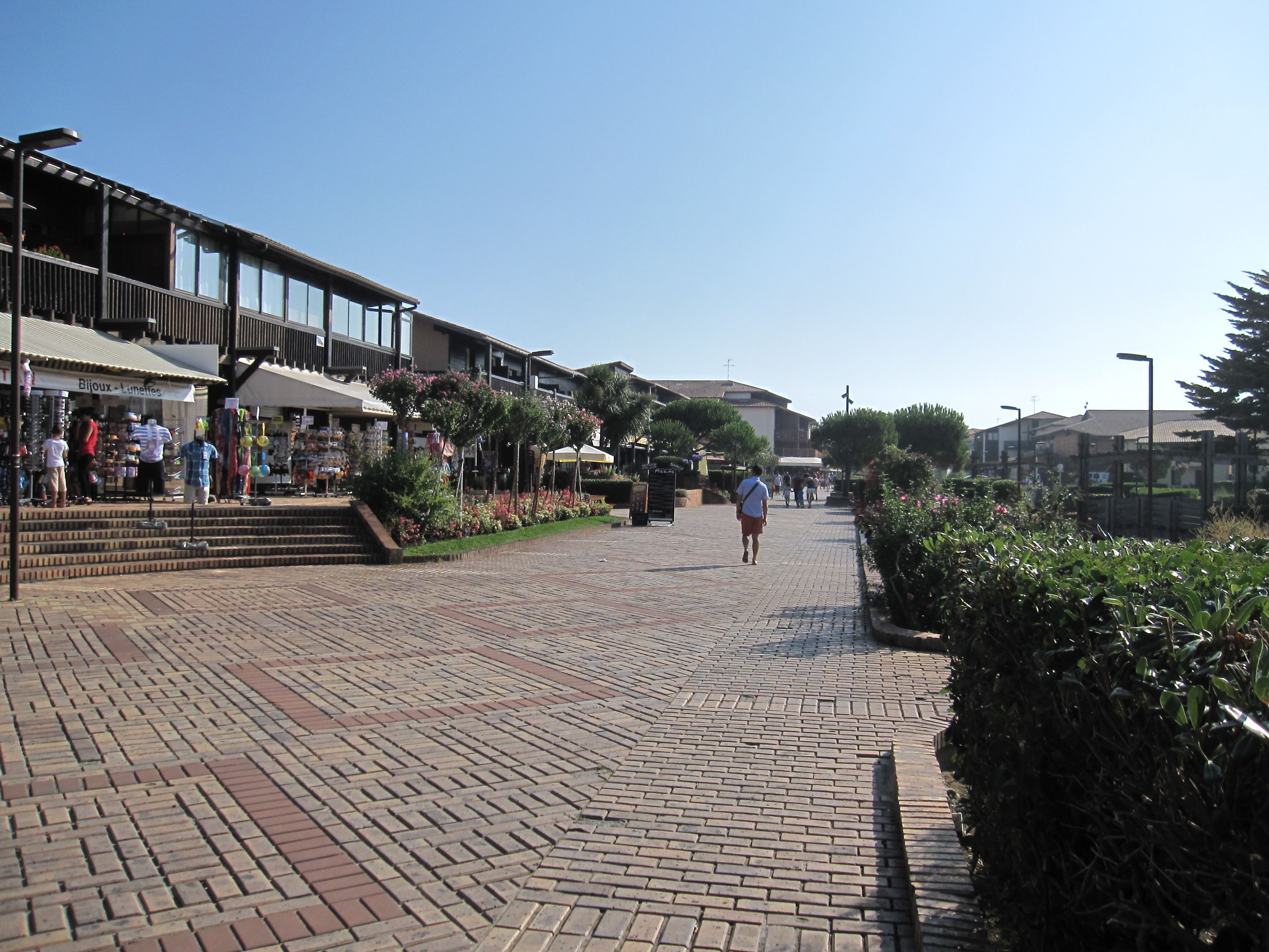 A paved walkway with shops on one side and a building with a balcony on the other.