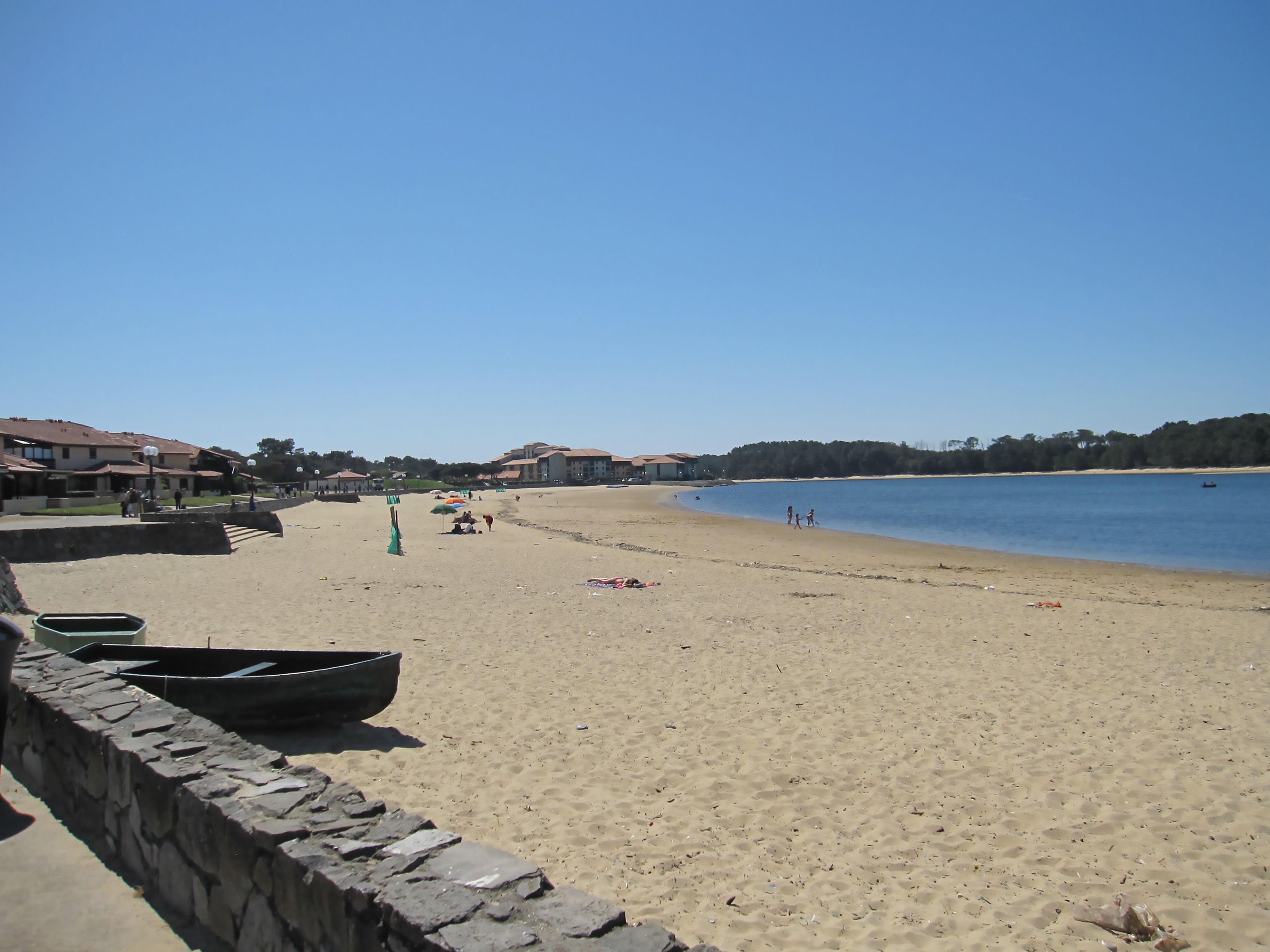 A beach with a stone wall, a row of houses, and a calm sea.