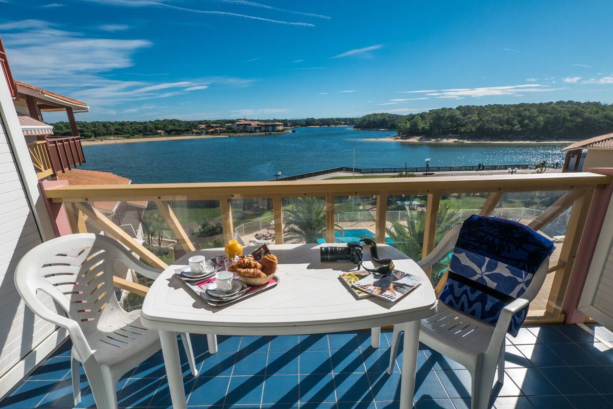 A balcony with a table set for breakfast, overlooking a body of water and a beach.