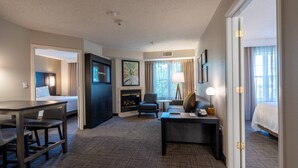 A hotel room with a bed, a desk with a lamp, a sofa, a fireplace, and a large window with curtains. - Residence Inn by Marriott Princeton at Carnegie Center (Princeton)