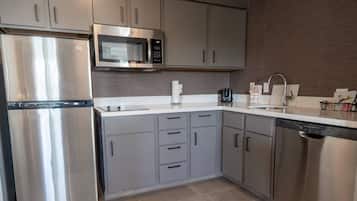 Een moderne keuken met roestvrijstalen apparatuur, grijze kastjes en een wit aanrecht.