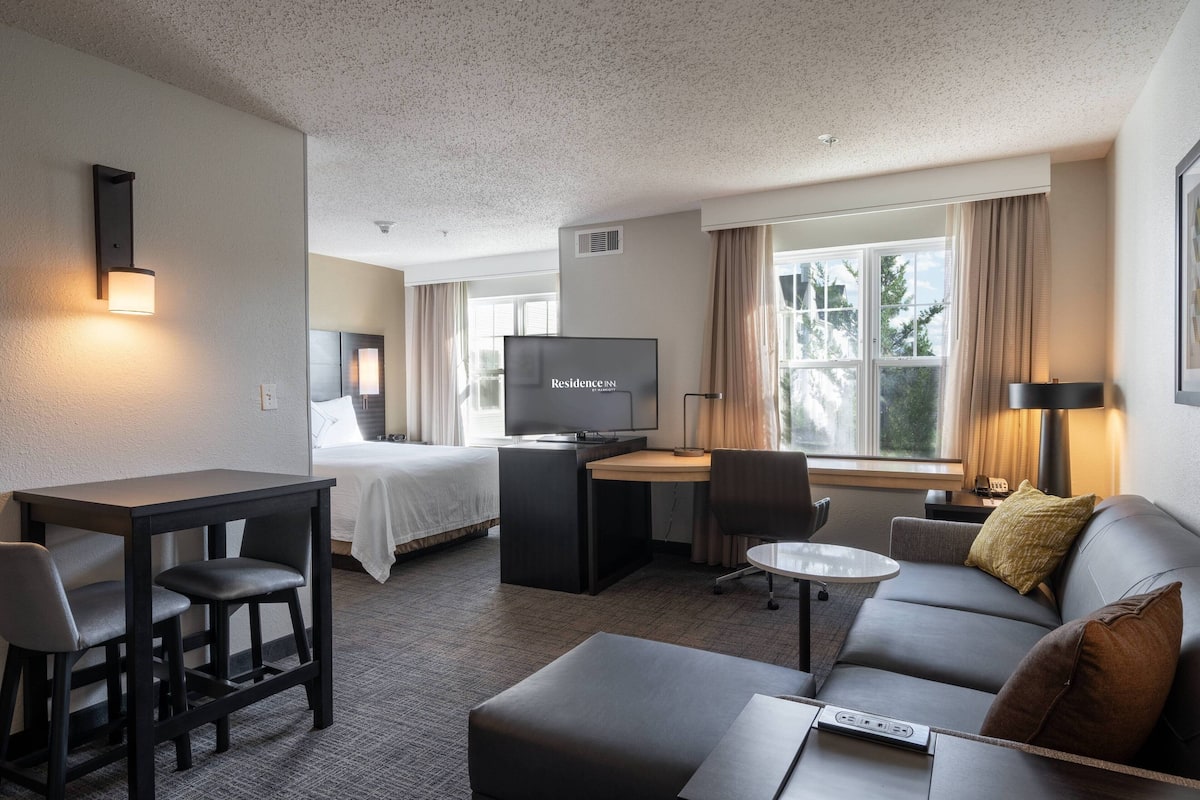 A hotel room with a bed, a desk with a computer, a sofa, and a TV.