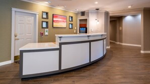A reception area with a curved reception desk, a wall-mounted artwork, a refrigerator, and a door. - Residence Inn by Marriott Princeton at Carnegie Center (Princeton)