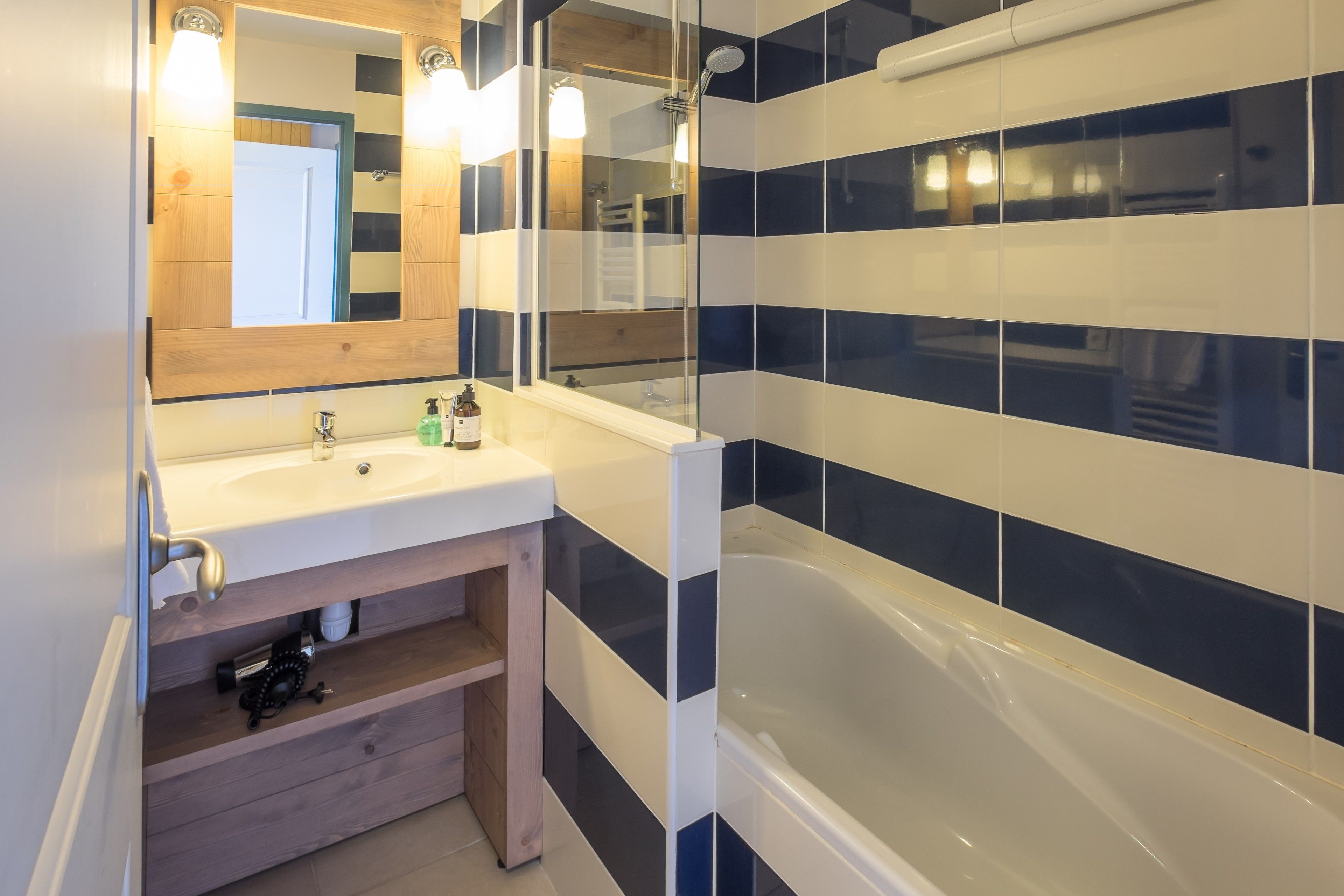 Een moderne badkamer met een witte wastafel, een houten opbergmeubel en een douchecabine met glazen wanden.