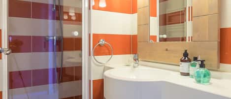 Un baño con ducha, lavamanos y espejo.