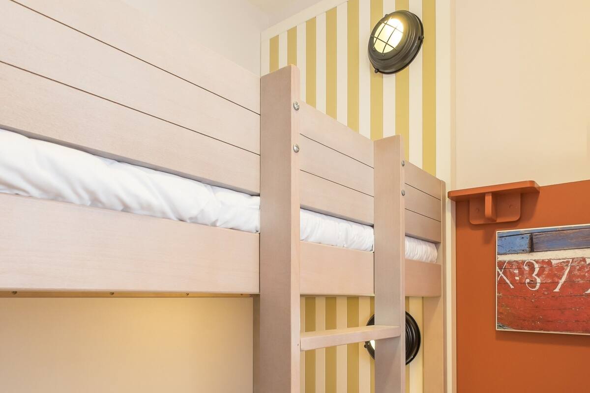 A bunk bed with a ladder, a small table, and a wall-mounted light fixture.