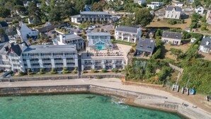 Luchtbeeld van een kustplaats met een opvallend hotel, inclusief een zwembad, omringd door woongebouwen en een heldere waterlijn.