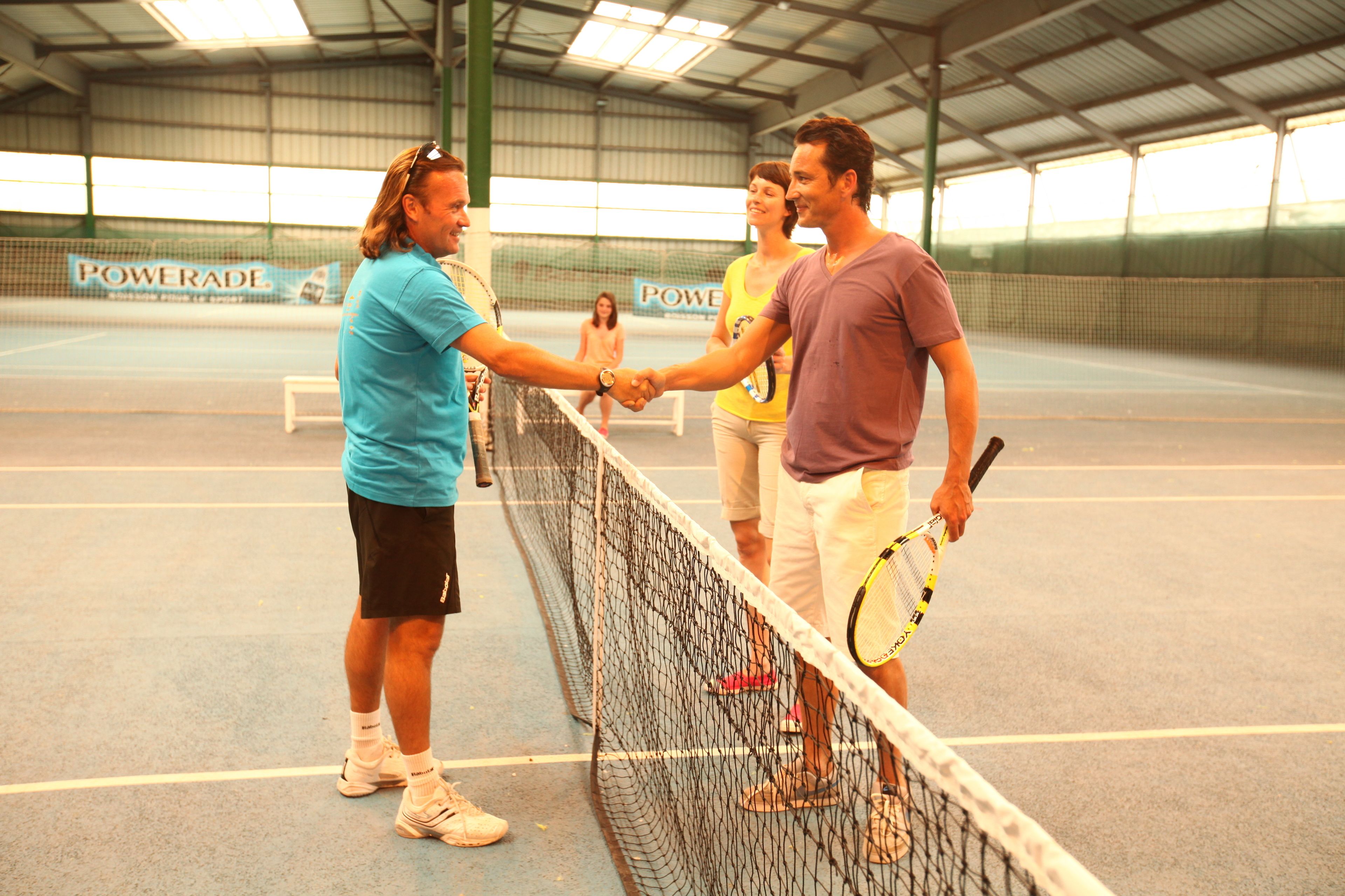 Ein Tennisplatz mit Netz, eine Powerade-Werbung und eine Gruppe von Menschen, die einander die Hand geben.