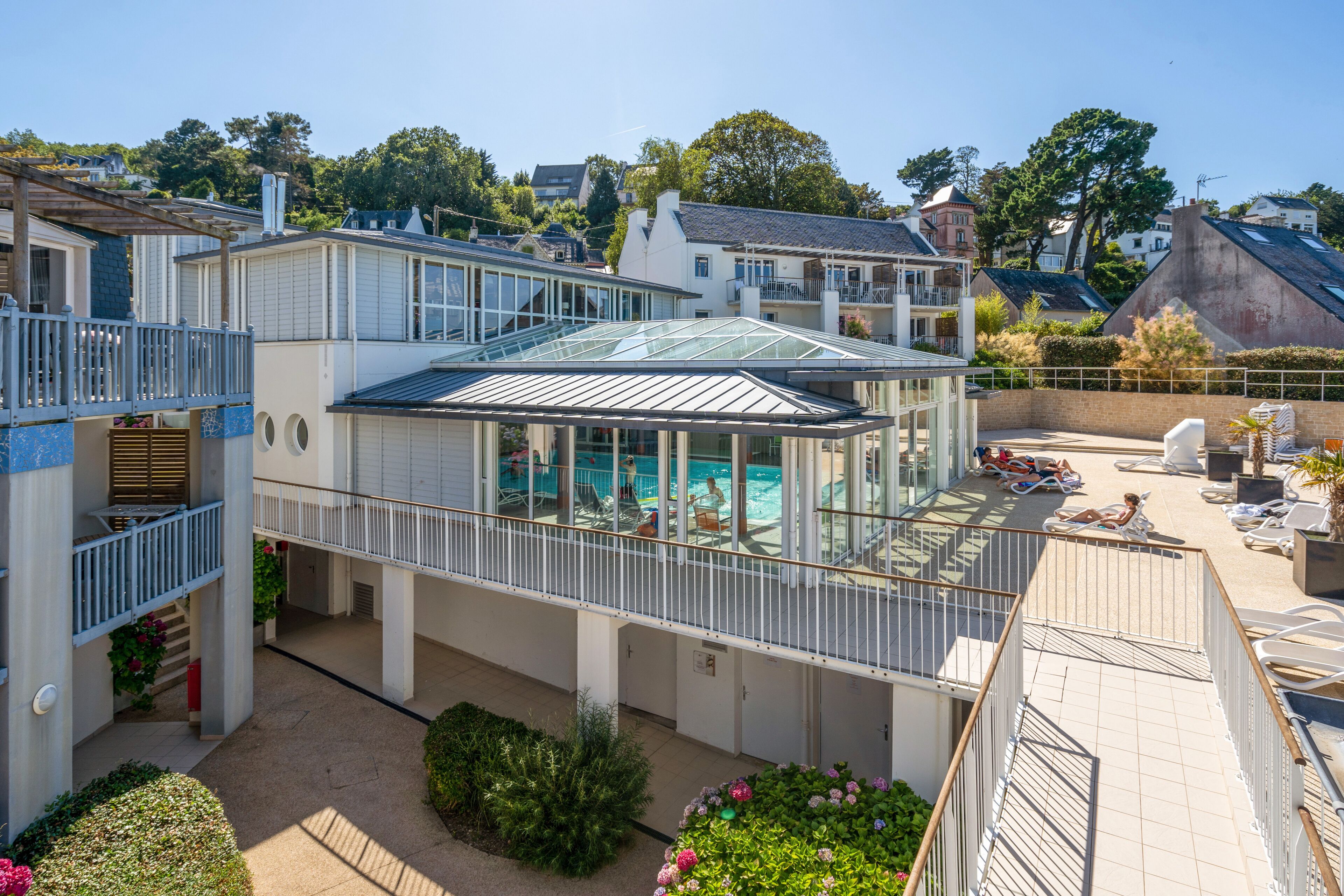 A residential building with a glass-enclosed swimming pool, a covered patio area, and a balcony with a railing.
