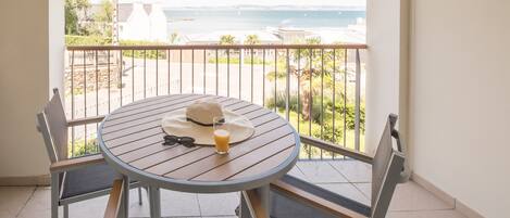 A balcony with a round table, chairs, a hat, and a glass of orange juice.