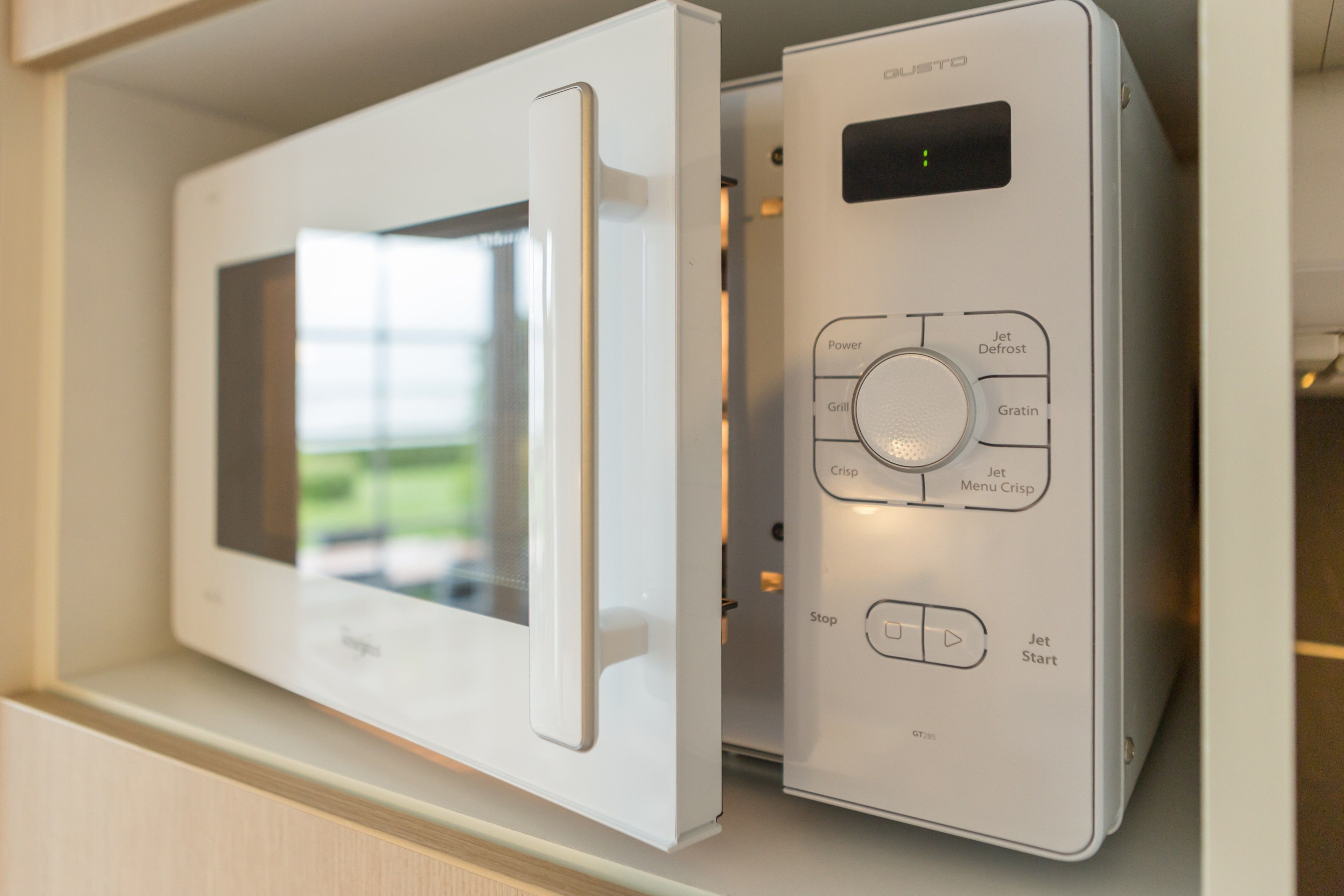 A microwave with a digital display and control panel, placed inside a kitchen cabinet.