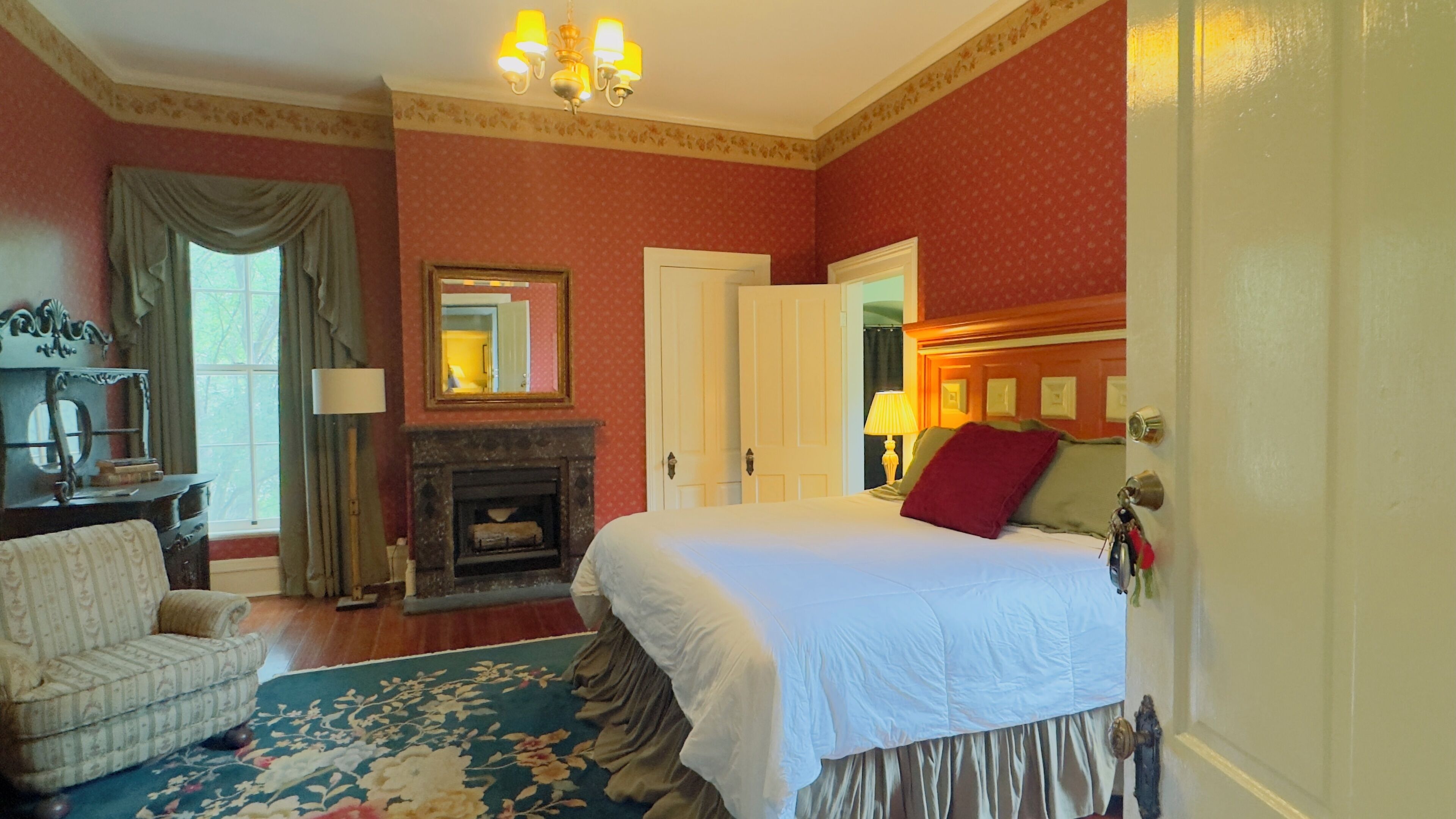 A hotel room with a bed, a chair, a fireplace, and a mirror.