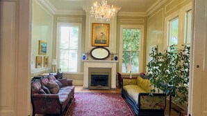 A room with a fireplace, two sofas, a chandelier, and a large window. - Rothschild-Pound House Inn (Columbus)