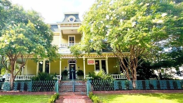 A two-story building with a balcony, surrounded by trees and a decorative fence. - Rothschild-Pound House Inn (Columbus)