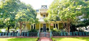 A two-story building with a balcony, surrounded by trees and a decorative fence.