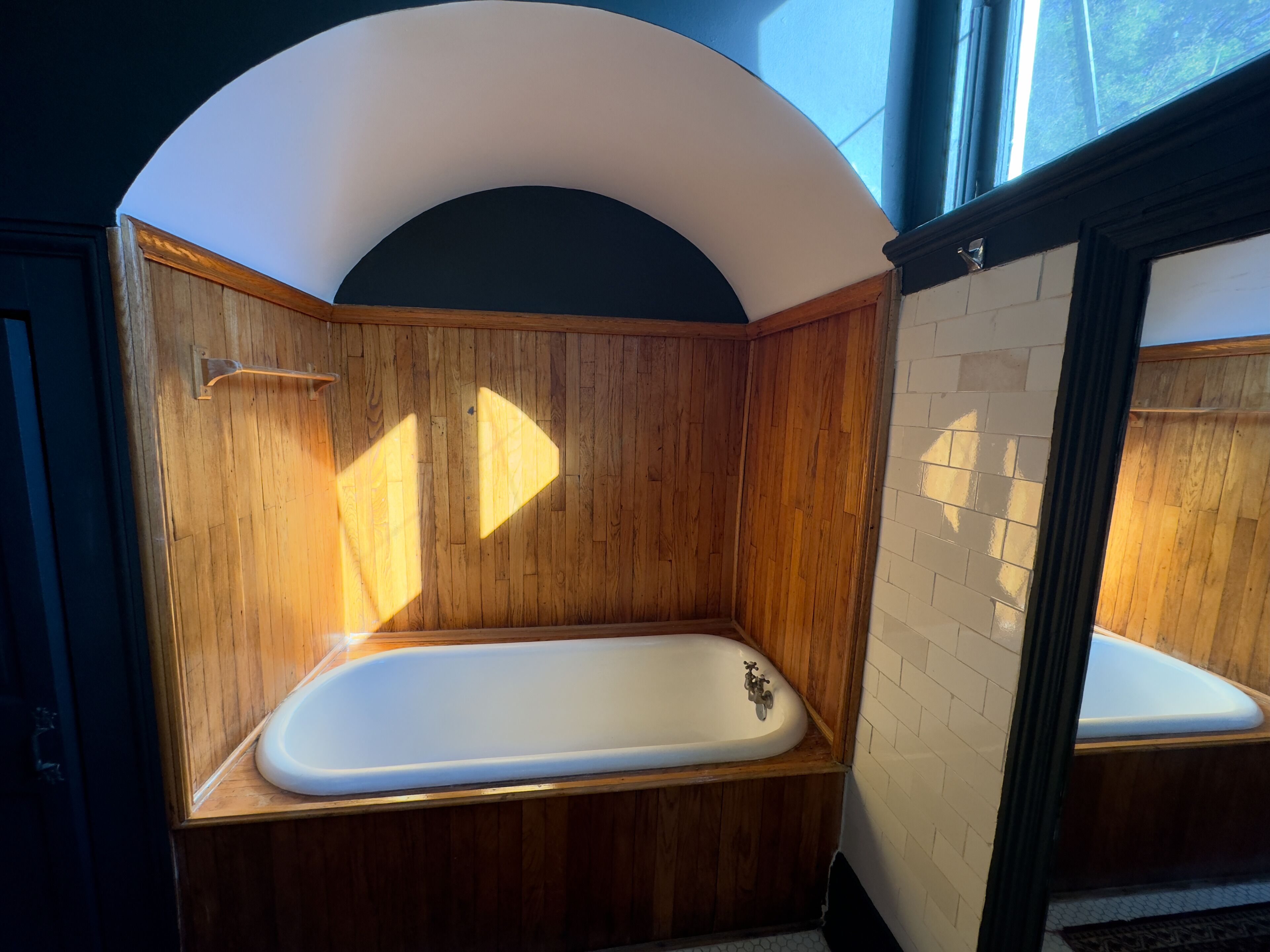 A wooden bathtub with a white interior, a wooden wall, and a white tiled floor.