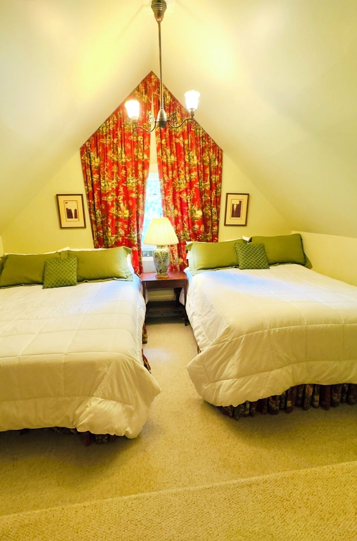 A bedroom with two beds, a chandelier, and a window with red curtains.
