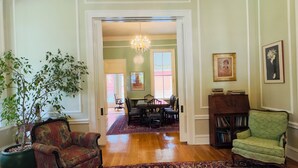 A spacious living room with hardwood flooring, a dining area with a chandelier, and a green armchair. - Rothschild-Pound House Inn (Columbus)