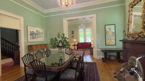 A dining room with a glass-top table, wooden chairs, a red sofa, and a chandelier. - Rothschild-Pound House Inn (Columbus)