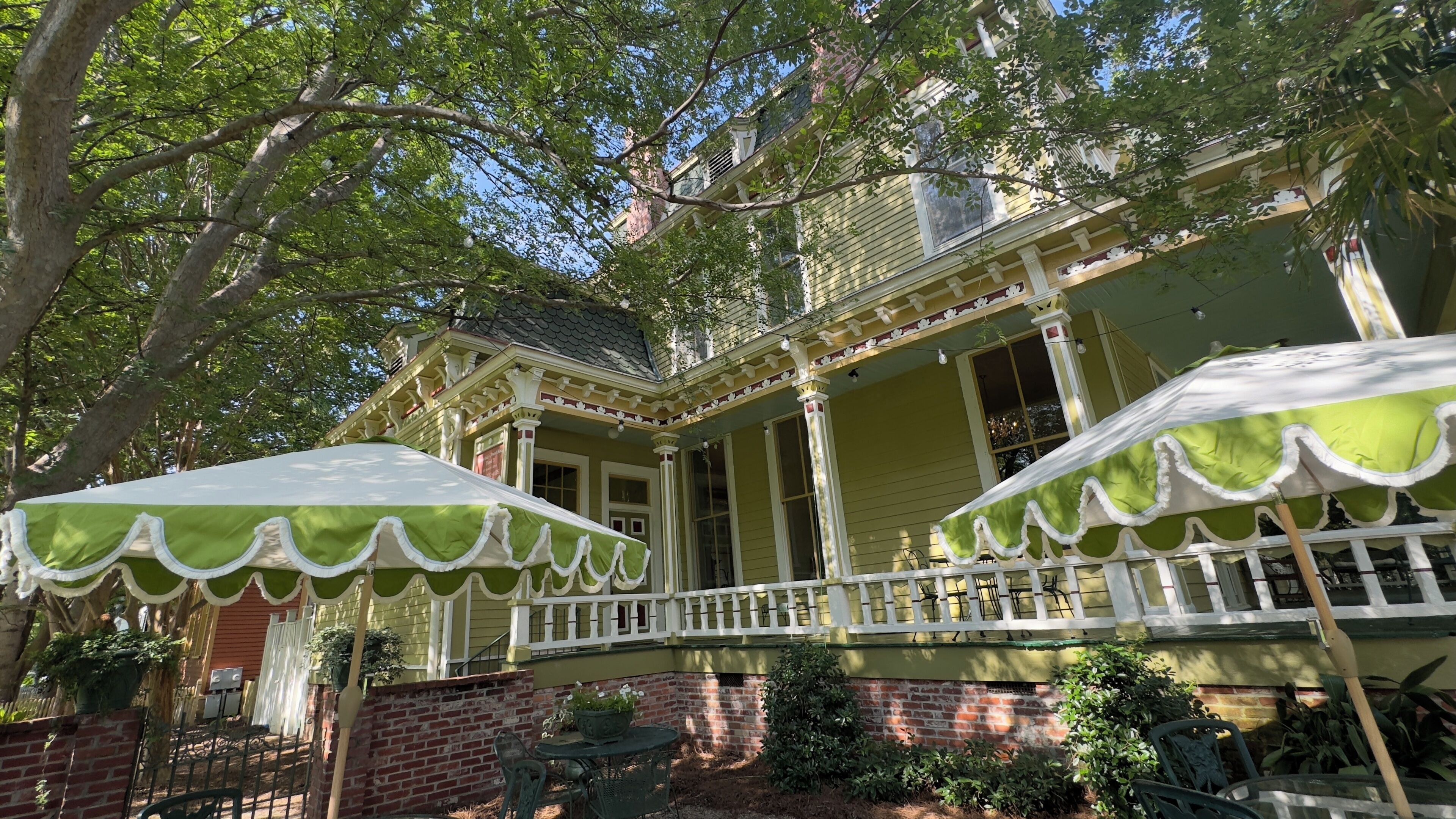 A two-story house with a porch, green and white exterior, and a brick foundation.