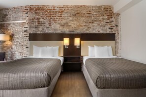A hotel room with a brick wall, two beds with matching headboards, bedside lamps, and a wooden floor.