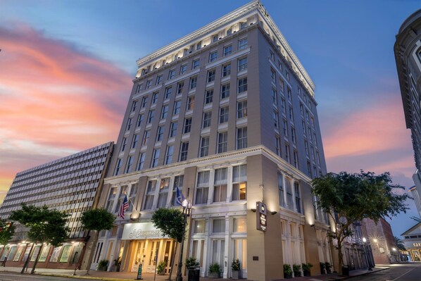 A multi-story hotel with a classic architectural style, featuring a prominent corner entrance, large windows, and a flagpole with the American flag.