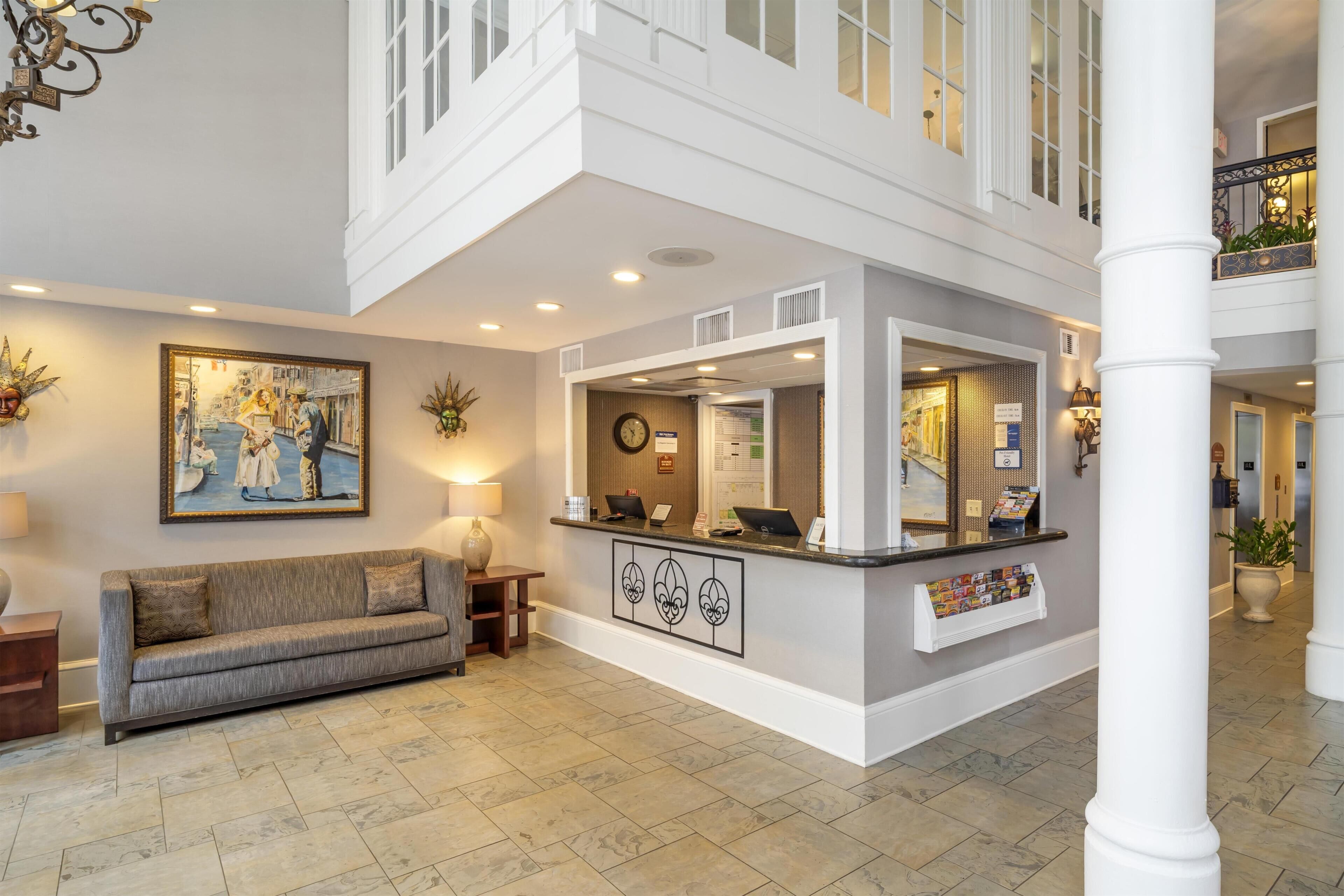 A hotel lobby with a reception desk, a sofa, a painting, and a staircase.