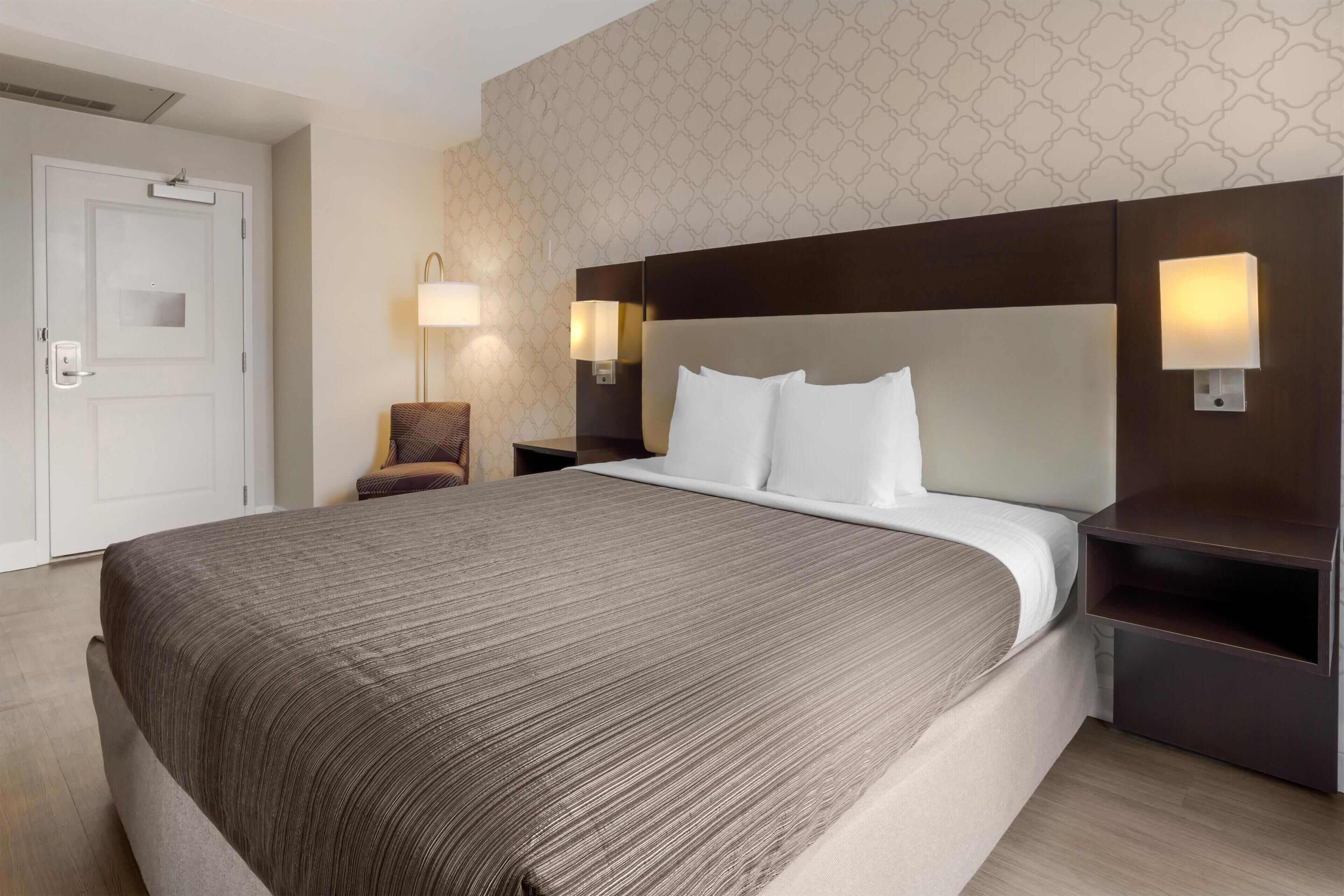 A hotel room with a large bed, two bedside tables with lamps, a chair, and a door.