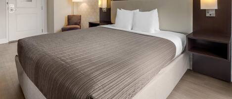 A hotel room with a large bed, two bedside tables with lamps, a chair, and a door.